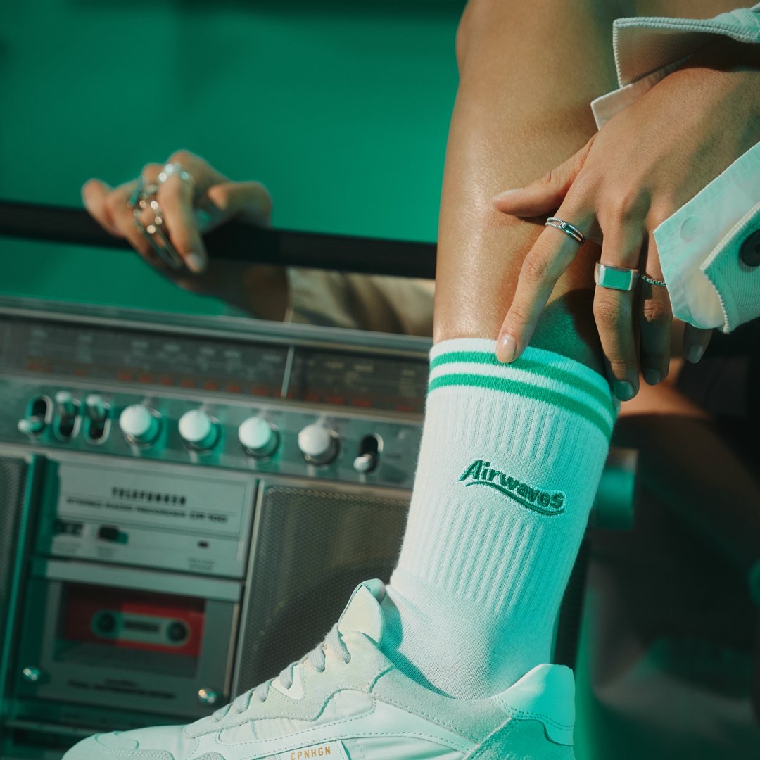 Grüne Airwaves-Socke mit weißen Streifen in einem weißen Sneaker, daneben das Rücklicht eines Autos