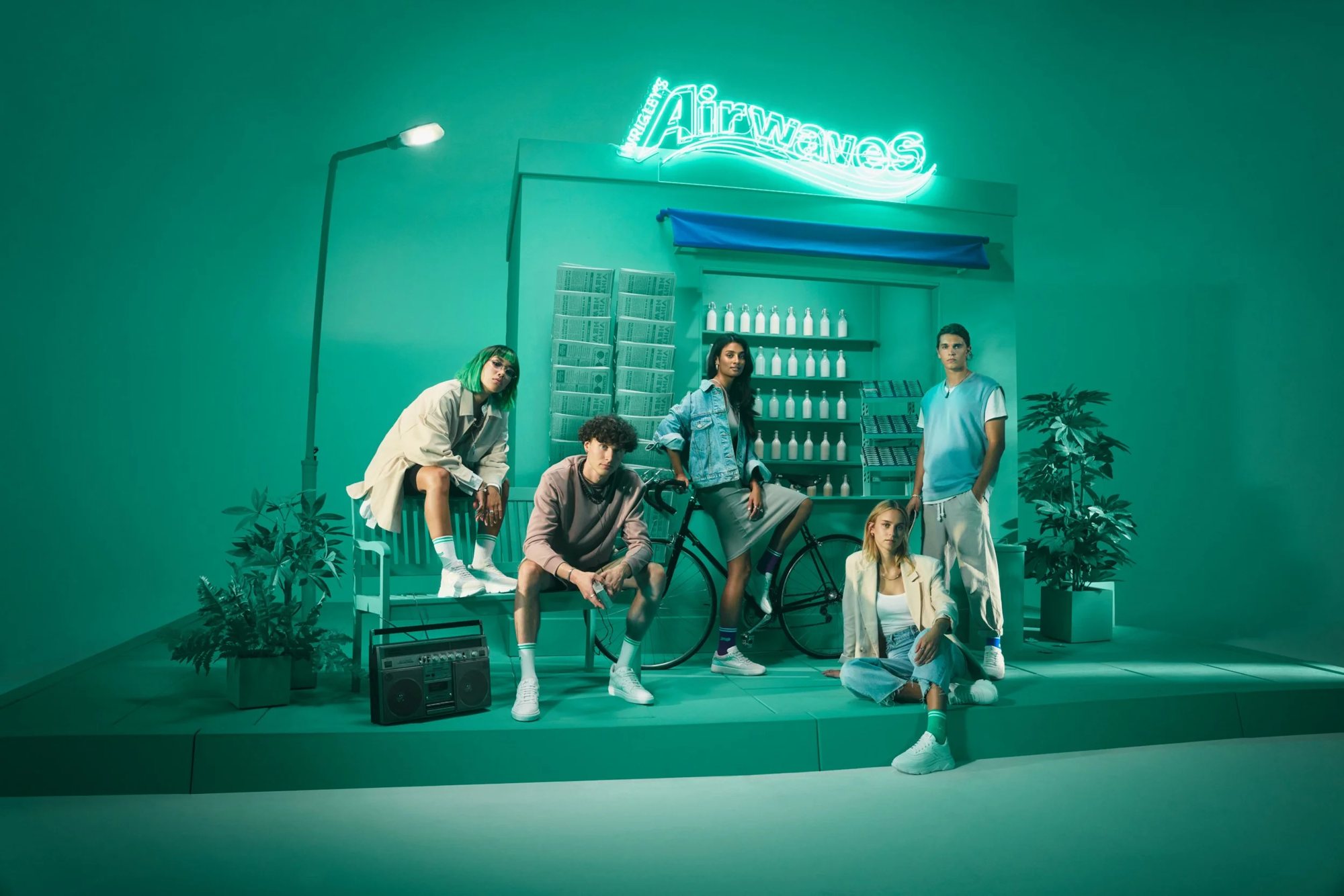 Fünf junge Leute vor dem mintgrünen Kiosk-Set mit Airwaves-Neonschriftzug, Fahrrad und Ghettoblaster
