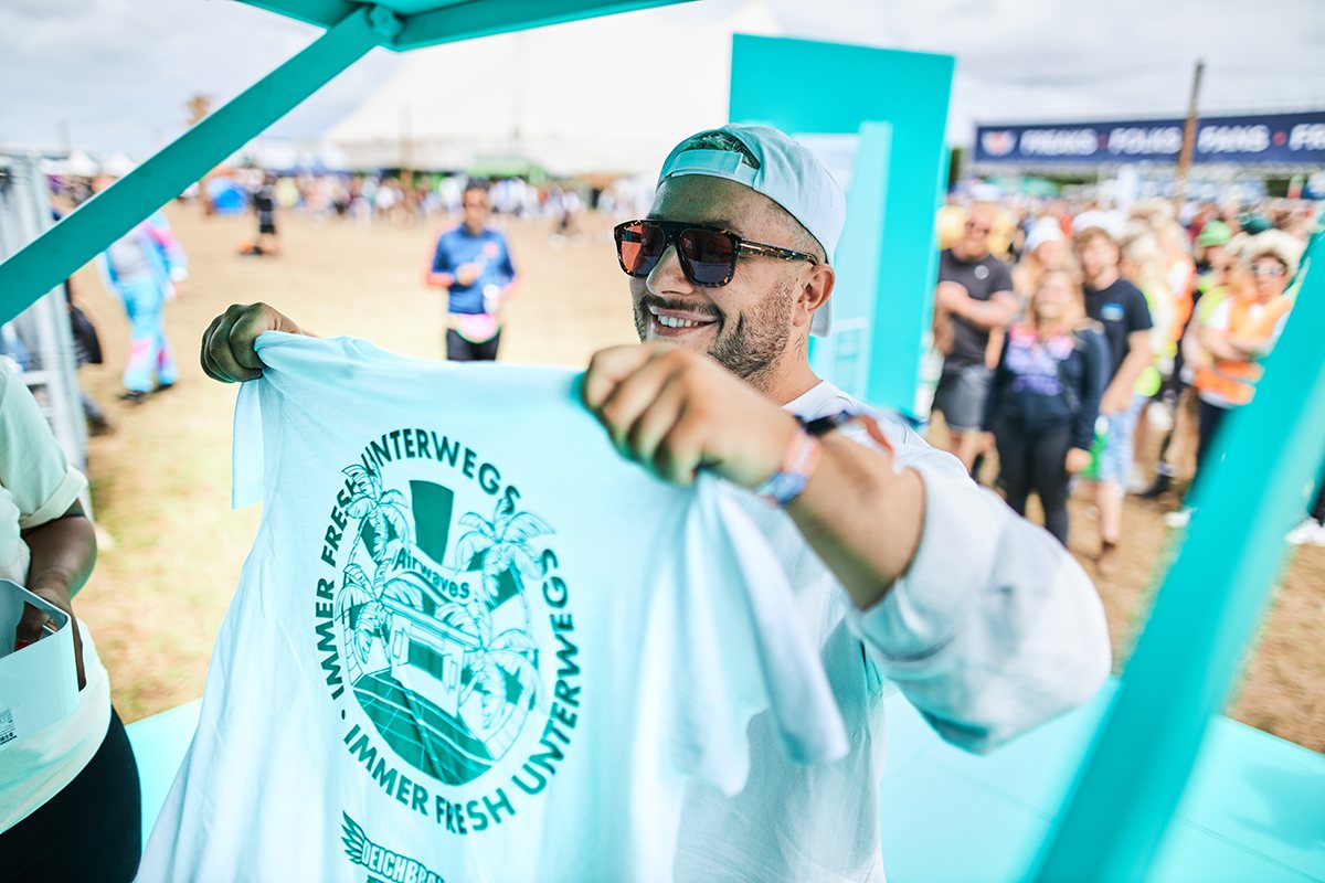Ein Gast hält ein Shirt mit dem Aufdruck „Immer fresh unterwegs“ hoch