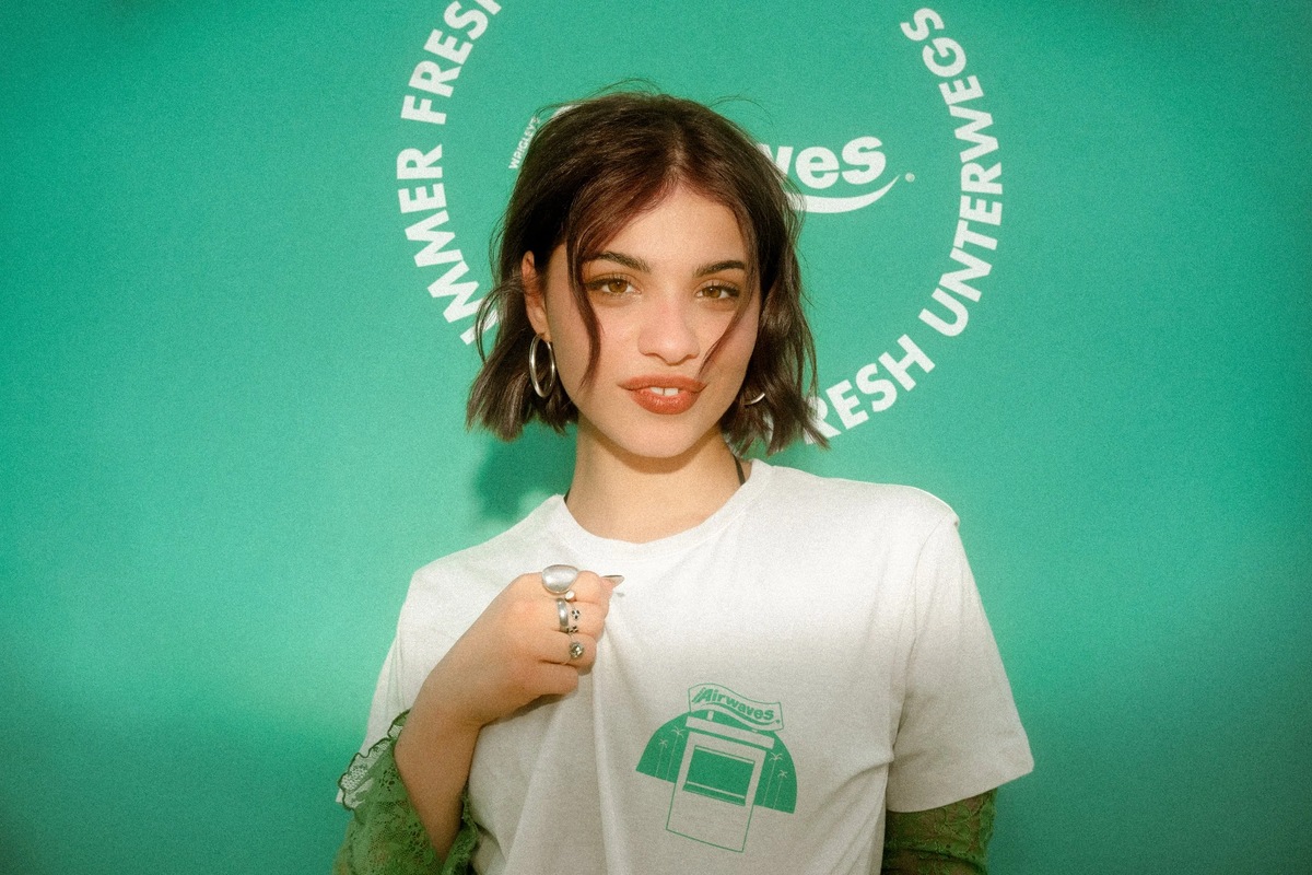 Eine Frau im Airwaves-Shirt vor einer mintgrünen Wand mit dem Slogan