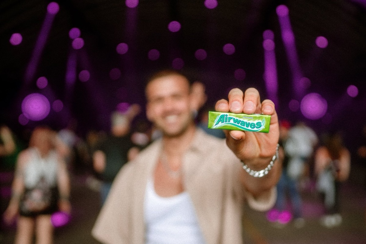 Ein Gast hält eine Packung Airwaves vor violetten Bühnenlichtern in die Kamera