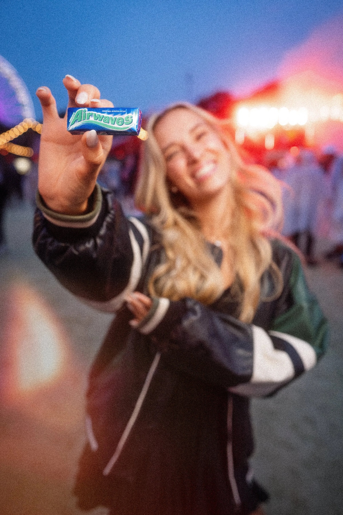 Eine junge Frau hält Airwaves in die Kamera, dahinter Festivallichter