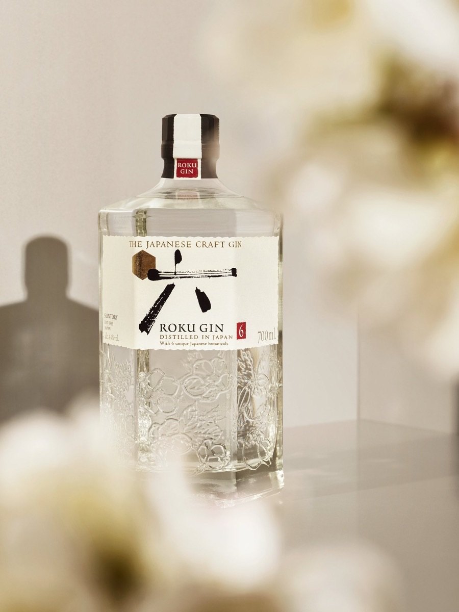 Die Flasche Roku Gin hinter unscharfen weißen Blüten