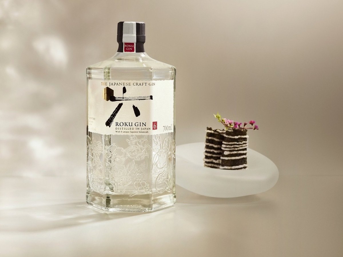 Die Flasche Roku Gin neben einem kleinen Dessert auf hellem Grund