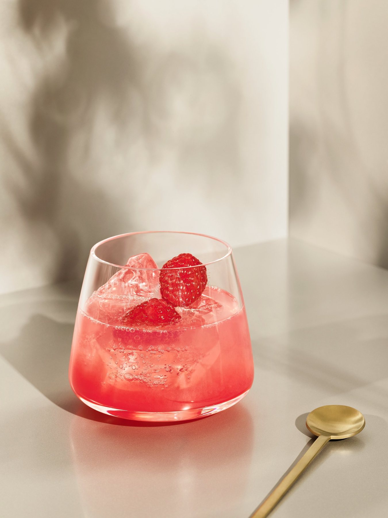 Roter Drink mit Roku Gin und Sakura-Blüte, daneben ein goldener Löffel